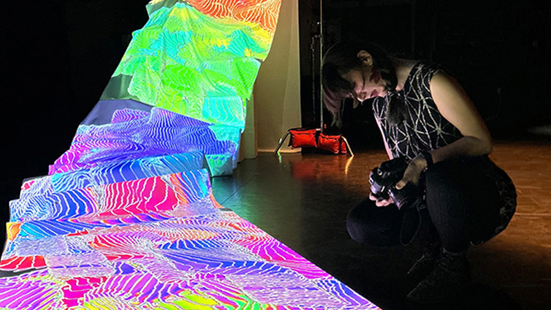a student kneels next to a hyper colorful artwork
