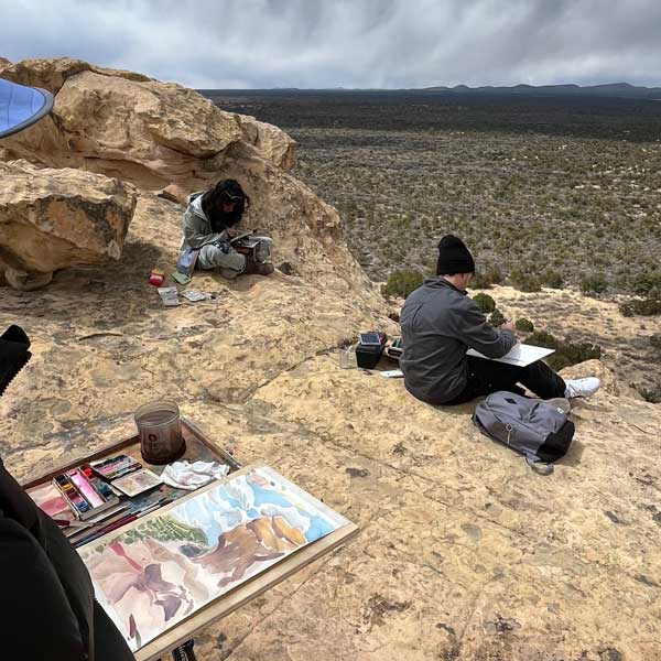 Photo of people sitting overlooking the desert and painting the scenery