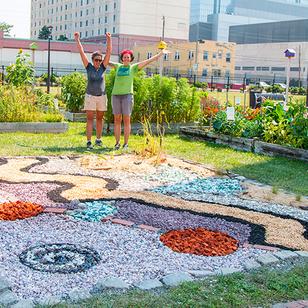 two students with arms raised with completed outdoor artwork in a garden
